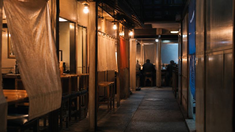 駅の建物の中の飲食店の小路。裸電球と暖簾が並ぶ（イメージ）